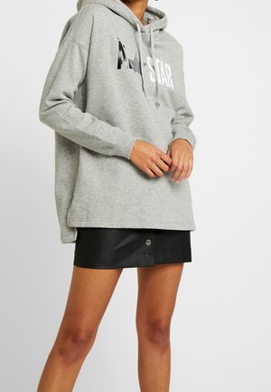 Grauer, übergroßer Hoodie aus weichem Stoff mit einem Front-Graphic, das das Wort "STAR" und einen Stern zeigt. Kombiniert mit einem schwarzen Leder-Minirock.