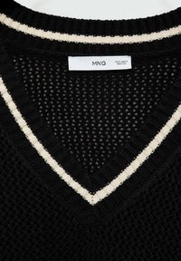 Pull en maille noire avec un col en V, présentant un motif texturé et des rayures de couleur crème le long de l'encolure. Étiquette de la marque visible.