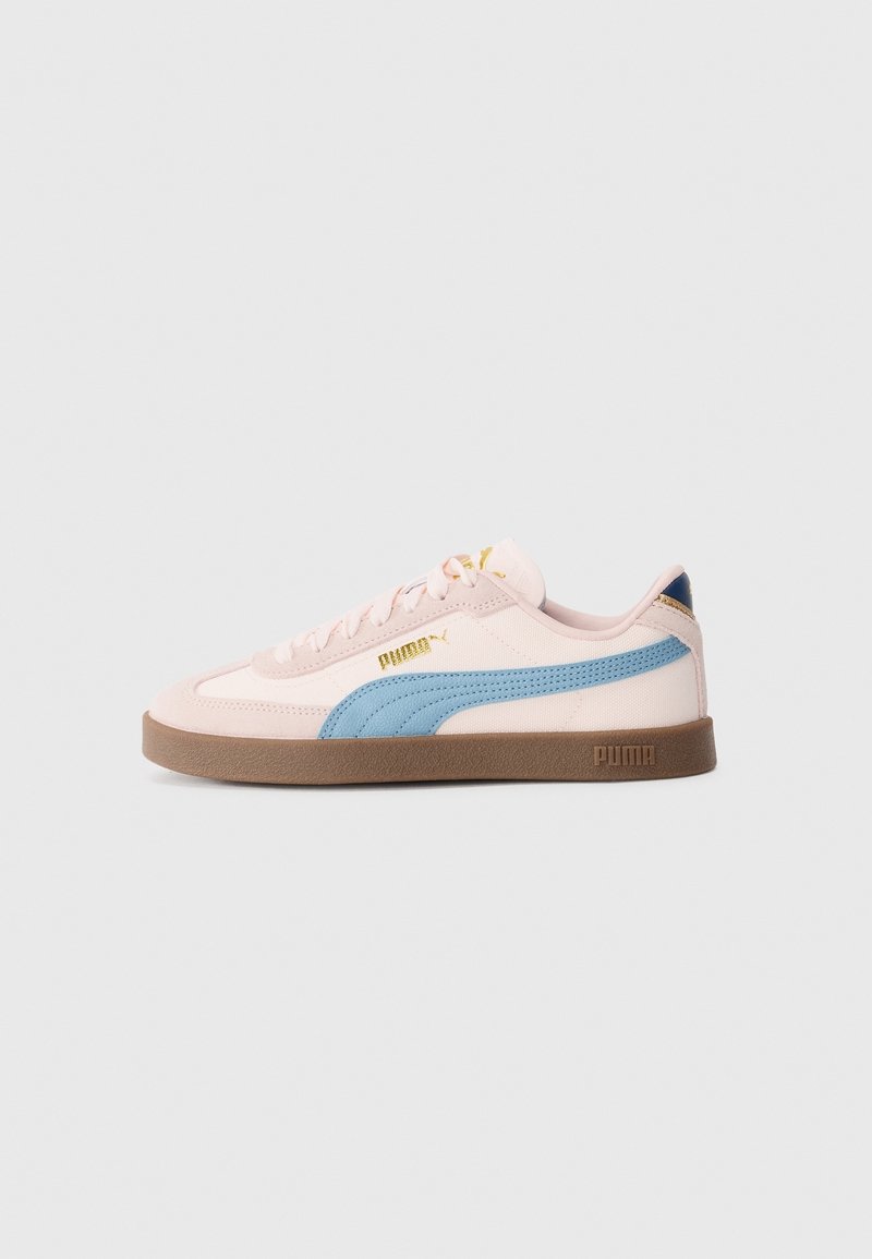 Baskets basses Puma avec dessus beige, bande latérale bleue, semelle marron et logo doré sur un fond uni gris clair.