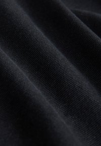 Gros plan d'un tissu noir avec une texture de tissage diagonale visible et des plis doux.