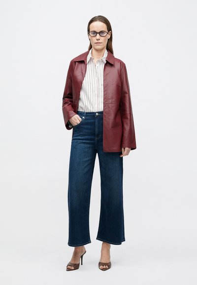 Bordó bőr dzseki kiképzett gallérral, fehér csíkos inggel és széles szárú sötét farmernadrággal párosítva. A megjelenést barna magassarkú papucs teszi teljessé.