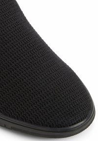 Czarne dzianinowe buty wsuwane o teksturowanej powierzchni, z okrągłym noskiem i gumową podeszwą. Charakteryzują się minimalistycznym designem i brakiem widocznych elementów metalowych.