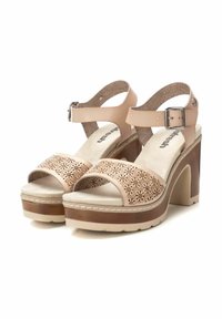 Sandalias de plataforma beige con parte superior perforada, correa ajustable en el tobillo, plantilla acolchada y un tacón grueso con un acento marrón.