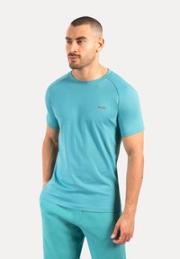 T-shirt turchese a maniche corte realizzato in tessuto leggero, con colletto a girocollo e un discreto logo sul petto. Texture liscia.