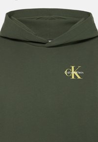 Hanorac din bumbac verde măsliniu, cu buzunar frontal și glugă cu șnur, având un logo galben 'Calvin Klein' pe pieptul din stânga.