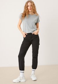 Szara koszulka z krótkim rękawem, czarne spodnie cargo z bocznymi kieszeniami, elastyczne mankiety, noszone z białymi sneakersami i paskowanymi skarpetami do kostek.