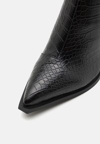 Bottine noire en similicuir texturé avec un bout pointu et une semelle épaisse noire présentant un subtil motif crocodile.