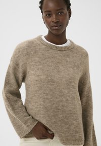 Pull en laine beige à coupe décontractée, col rond et poignets côtelés. Texture douce, avec des détails discrets le long de l'ourlet.