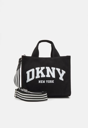 Mała czarna torba typu tote z krótkimi uchwytami, białym logo DKNY New York oraz odpinanym czarno-białym paskiem na ramię w paski.