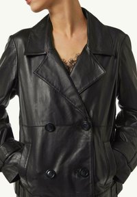 Schwarze, doppelt geknöpfte Lederjacke mit Reverskragen, zwei großen Knöpfen, Seitentaschen und glatter Textur. Spitzendetail ist darunter sichtbar.