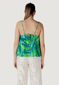 Top sin mangas con estampado verde y diseño de lazo en la espalda, hecho de material ligero, combinado con pantalones blancos de pierna ancha y textura.