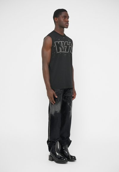 Fekete ujjatlan póló nagy "KYZ" felirattal, fekete kopott farmer oldal dekorációkkal, és fényes fekete bokacsizma.