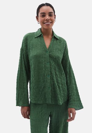 Camicia verde strutturata con colletto, maniche lunghe e chiusura con bottoni. Il tessuto presenta un motivo stropicciato, abbinato a pantaloni coordinati.
