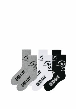 Drei Paar Socken in Grau, Weiß und Schwarz, jeweils mit einer Gleitschirm-Grafik und dem Wort "CHIEMSEE" auf Fuß und Bein bedruckt.