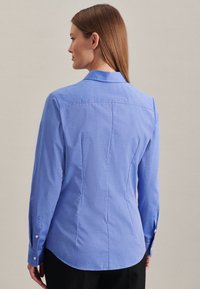 Aansluitend blauw overhemd met lange mouwen, met knoopmanchetten en een rugnaad detail. Glad stof met subtiele textuur.