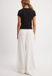 Must have must maap black cotton short sleeves t-särk, mis on paari pandud valgete laiade pükstega, mis on valmistatud tekstuursest, kootud kangast. Pükstel on kogutud elastne vöö.