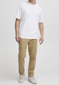 T-shirt en coton blanc avec un col rond classique, associé à un pantalon chino beige clair et à des baskets blanches. Design minimaliste et coupe décontractée.