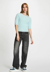 Maglione corto a maniche corte di colore azzurro chiaro e morbido abbinato a jeans a gamba larga grigio scuro. Il maglione presenta un collo rotondo e dettagli con bottoni sulle maniche.