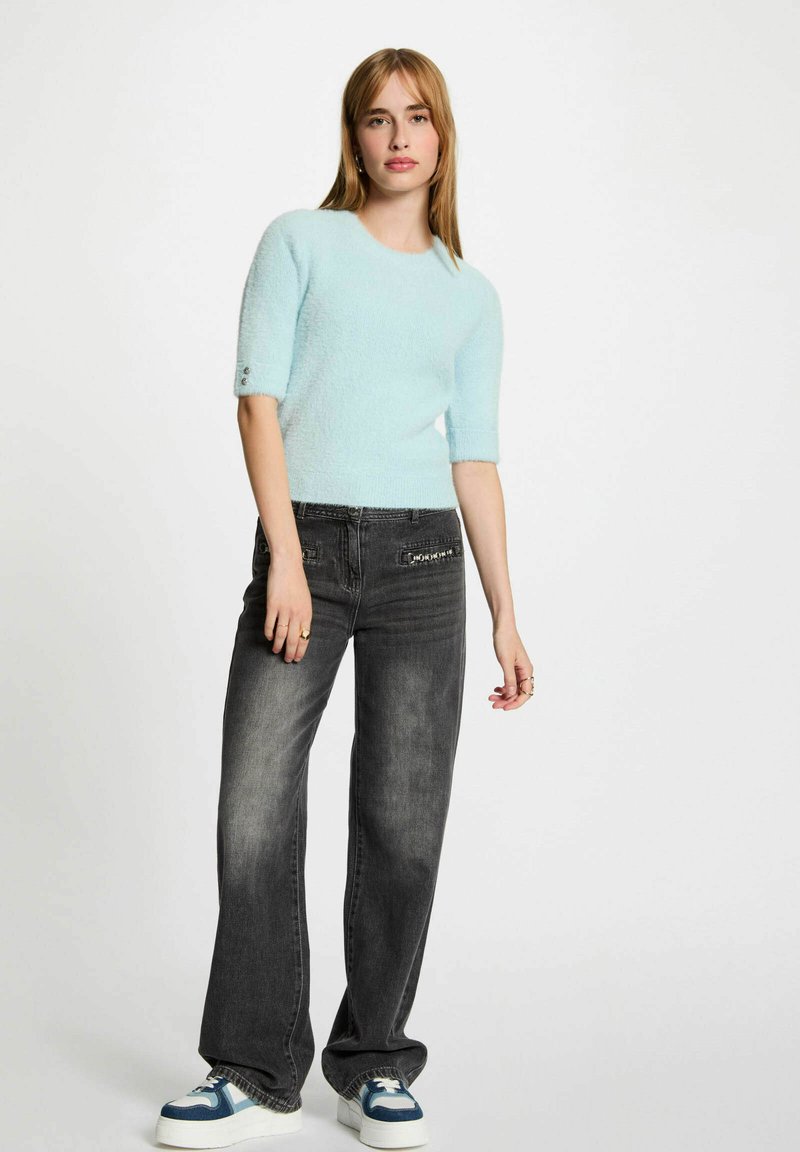 Maglione corto a maniche corte di colore azzurro chiaro e morbido abbinato a jeans a gamba larga grigio scuro. Il maglione presenta un collo rotondo e dettagli con bottoni sulle maniche.