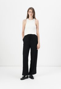 Witte mouwloze top gecombineerd met losse zwarte broeken. De broeken hebben een elastische tailleband en zijzakken. Zwarte schoenen maken de outfit compleet.