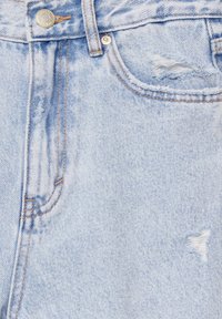 Il tessuto in denim blu chiaro presenta una texture sbiadita con aree sfrangiate e cuciture arancioni a contrasto vicino alle tasche e alla chiusura.