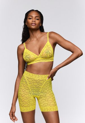 Gele kanten bralette en bijpassende korte leggings. Doorzichtig kanten materiaal met bloemenpatronen en verstelbare bandjes. Slank aansluitend ontwerp.