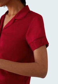 Red blouse with a collared neckline and short sleeves featuring floral lace trim. Smooth texture with a fitted silhouette.