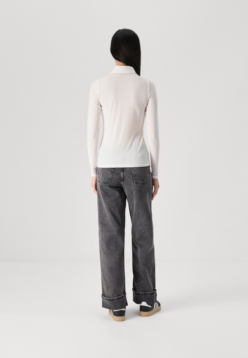 Langärmliges, helles Oberteil mit Kragen, kombiniert mit lockeren, dunkelgrauen Jeans und lässigen Sneakers. Sanfte Textur, entspannter Schnitt.