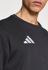 Σκούρα γκρι φούτερ με στρογγυλή λαιμόκοψη και απαλή υφή, με λευκό λογότυπο τριών λωρίδων στο στήθος.