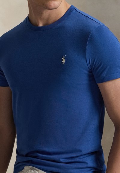 Κοντομάνικο μπλε μπλουζάκι από απαλό ύφασμα με στρογγυλή λαιμόκοψη. Διαθέτει ένα μικρό, κεντημένο λογότυπο στο αριστερό στήθος.