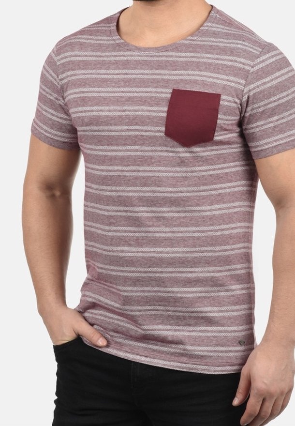 Homme portant un t-shirt à manches courtes rayé mauve et blanc avec une poche poitrine unie bordeaux, associé à un pantalon noir.