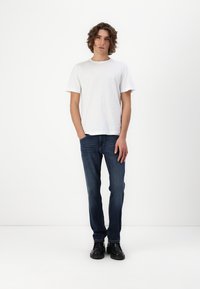 Hvid bomulds T-shirt, afslappet pasform, korte ærmer. Mørkeblå jeans, lige snit. Sorte sko, glat tekstur, simpel design.