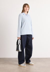Polo shirt a maniche lunghe di colore blu chiaro a righe con colletto, abbinato a pantaloni larghi in denim scuro. Tiene una piccola borsa argentata. Calzature casual.