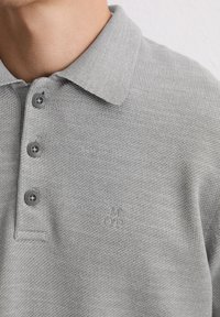 Szara koszulka polo z kołnierzykiem, teksturowana tkanina, trzy ciemne guziki oraz subtelne haftowane logo z lewej strony.