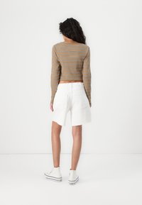 Top court rayé marron à manches longues, associé à un short en denim blanc avec un ourlet effiloché, porté avec des sneakers montantes blanches.