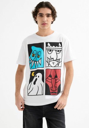 Camiseta blanca de algodón con cuatro caras estilo caricatura: un monstruo azul, un fantasma, una figura en blanco y negro, y una cara roja, con contornos gruesos y colores brillantes.