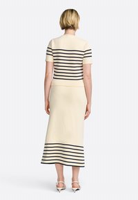 Ensemble tricot beige clair avec des rayures navy. Haut à manches courtes avec une taille cintrée, accompagné d'une longue jupe. Texture lisse, détails minimaux.
