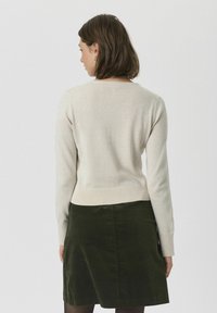 Un pull beige clair avec un col rond, une bordure côtelée et des manches longues, associé à une jupe verte foncée. Texture lisse, détails minimalistes.
