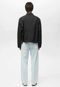 Zwarte croppedjas van gladde stof met een klassieke kraag en knoopmanchetten, gecombineerd met lichtblauwe wijde Jeans.