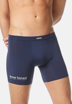Torso maschile che indossa boxer aderenti blu navy con il logo "bruno banani" e il testo "non per tutti" sulla coscia sinistra.