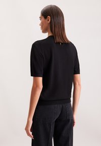 Czarny sweter z krótkim rękawem i okrągłym dekoltem, z małym otworem z tyłu, wykonany z miękkiego materiału, w połączeniu z ciemnymi dżinsami.