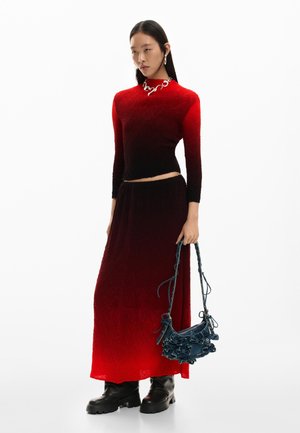 Woman wearing a red-to-black ombre long-sleeve top and matching skirt, holding a navy handbag with decorative bows, and black chunky boots.