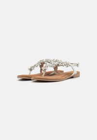 Flade sandaler med en brun ruskindsfod seng, sølvremme og blomsterudsmykninger med små hvide blomster og guldaccenter.