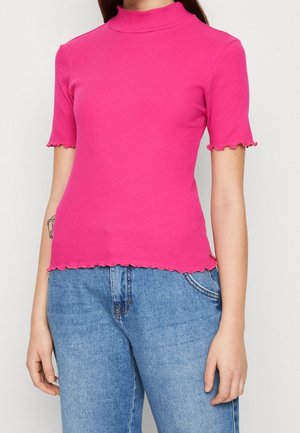 Haut rose ajusté à côtes avec un col montant et des manches courtes à bords festonnés, présentant un ourlet court et une texture douce. Porté avec des jeans bleus.
