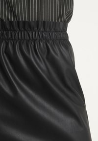 Falda de cuero negra con una cintura elástica fruncida y una textura suave, con detalles de rayas verticales en blanco y negro en la parte superior.