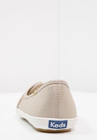 Baskets en toile beige au design bas, semelle en caoutchouc blanche et logo Keds bleu à l'arrière. Matériau texturé avec des coutures discrètes.