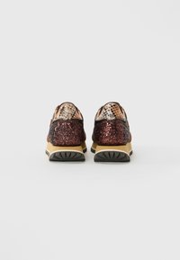 Une paire de baskets avec un talon pailleté brun foncé, une semelle beige et un accent en motif serpent sur l'onglet du talon, vue de l'arrière.