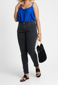 Modrá bezramínková blůza, černé džíny s vysokým pasem, černé klouzavé sandály a tkaná černá taška s dřevěnými uchy.