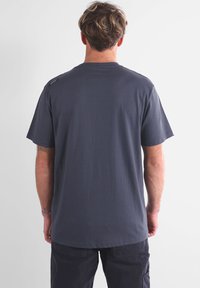 T-shirt en coton gris foncé à manches courtes, col rond, avec un accent logo sur l'épaule gauche. Texture lisse avec une coupe décontractée.