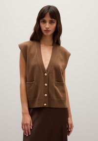 Braun gestrickte Weste mit kurzen Ärmeln, tiefem V-Ausschnitt, Knöpfen auf der Vorderseite und zwei Taschen. Weicher Stoff und lockere Passform.